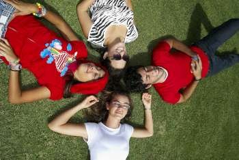 Three young women with a young man lying on grass and smiling