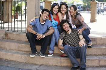 Two young men with three young women sitting on steps and smiling