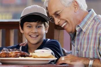 Close-up of a senior man with his grandson looking at a plate of food and smiling
