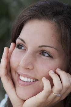 Close-up of a young woman smiling with her hands on her chin