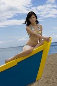 Young woman in bathing suit sitting on wooden boat on beach