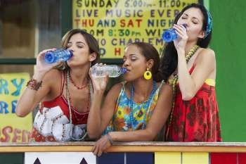 Three young women leaning on a railing and drinking water from bottles