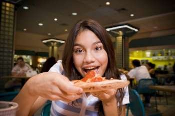 Teenage girl eating pizza in mall food court