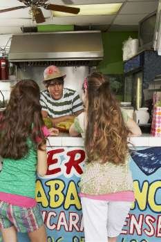 Rear view of two teenage girls talking to a bartender in a juice bar