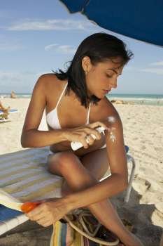 Young woman putting on sun tan lotion