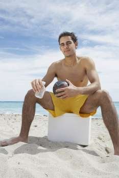 Portrait of a young man sitting on an ice box on the beach
