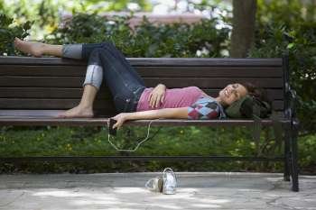 Young woman listening to an MP3 player and lying on a bench