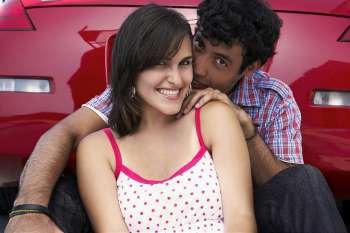 Portrait of a young couple sitting in front of a car