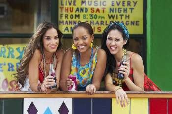 Portrait of three young women leaning on a railing and holding cold drinks