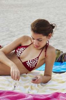 Young woman listening to music while sunbathing on beach