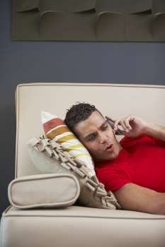 Side profile of a young man talking on a mobile phone and lying on a couch