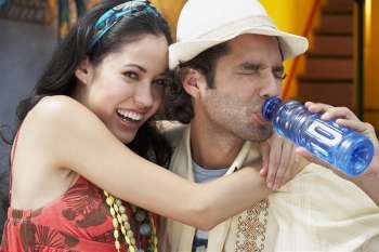 Close-up of a young woman smiling with a young man drinking water from a water bottle