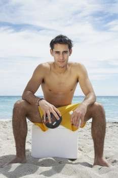 Portrait of a young man sitting on an ice box on the beach and holding a soccer ball