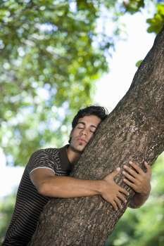 Young man hugging a tree trunk