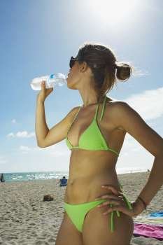Young woman drinking water on beach