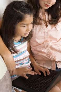 Side profile of a girl sitting with her mother and using a laptop