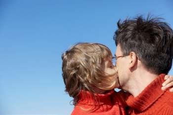 daughter kissing father on blue sky background