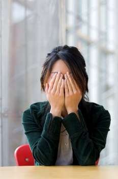 Asian woman covering eyes with her hands.