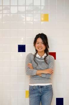 Young Asian girl standing against coloured tiled wall.