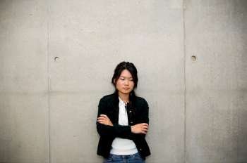 A single asian woman standing against cement wall.
