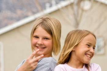Girls (8-11) gesturing with house in background, smiling, portrait