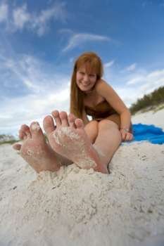 Barefoot girl sitting on beach, smiling, portrait