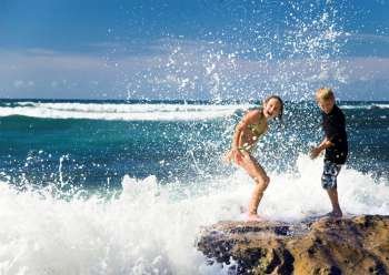 Children playing in ocean on rocks