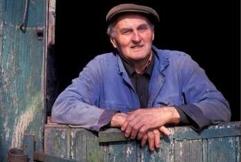 Senior man in cap posing in doorway of wooden barn