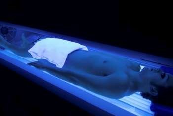 Bare chested man with eye protection laying in glowing light of tanning bed