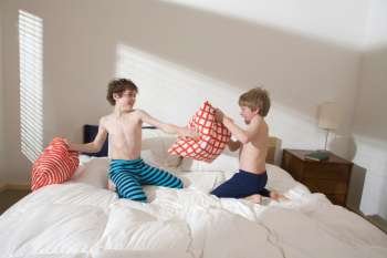 Bare chested brothers rough housing and pillow fighting on bed in bedroom