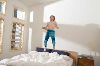 Bare chested boy playing and jumping in mid-air on bed in bedroom