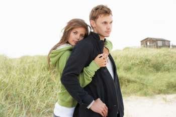 Romantic Young Couple Standing By Dunes With Beach Hut In Distance