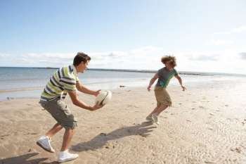 Two Teenage Boys Playing Rugby On Beach Together