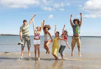 Group Of Teenage Friends Having Fun On Beach Together Jumping In Air