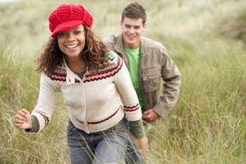 Teenage Couple Walking Through Sand Dunes Wearing Warm Clothing