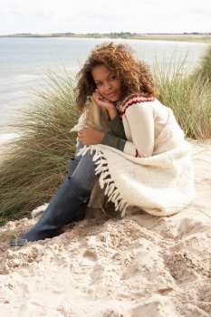 Young Woman Sitting In Sand Dunes Wrapped In Blanket