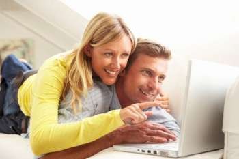 Couple Using Laptop Relaxing Sitting On Sofa At Home