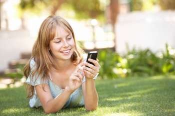 Teenage Girl Laying In Park Using Mobile Phone