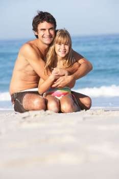 Father And Daughter Wearing Swimwear Sitting On Sandy Beach