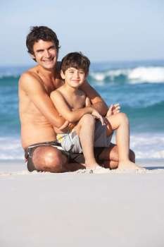 Father And Son Wearing Swimwear Sitting On Sandy Beach