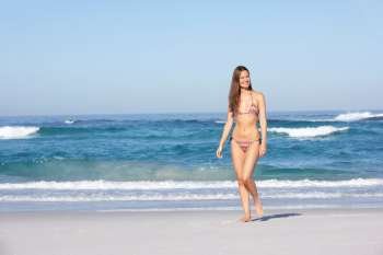 Young Woman Walking Along Sandy Beach On Holiday Wearing Bikini