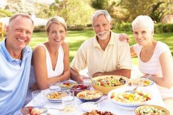 Adult Son And Daughter Enjoying Meal In Garden With Senior Parents