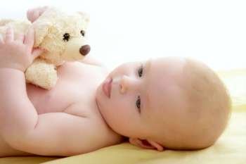 baby playing teddy bear laying on yellow bed 