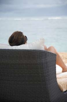 Back view of a woman sitting on a chaise chair on beach in Bali