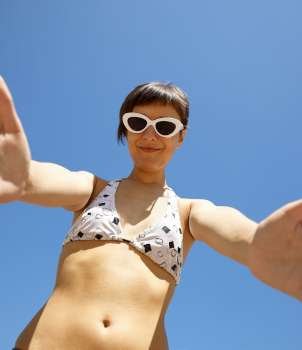 young adult in swimsuit, on the blue sky background, selective focus on sun-glasses