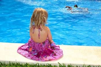 Little blond girl sitting rear back swimming pool outdoor