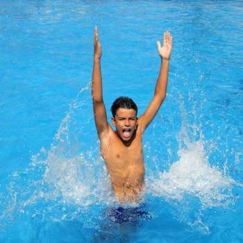 boy teenager splashing water open arms blue swimming pool