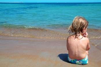 Little blond girl sit in beach shore looking turquoise ocean