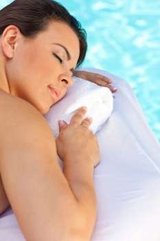 Portrait of a beautiful young Latina Hispanic woman eyes closed laying down and relaxing by a swimming pool at a health spa