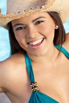 A sexy and beautiful young Latina Hispanic woman laughing in a bikini and straw cowboy hat with a swimming pool behind her